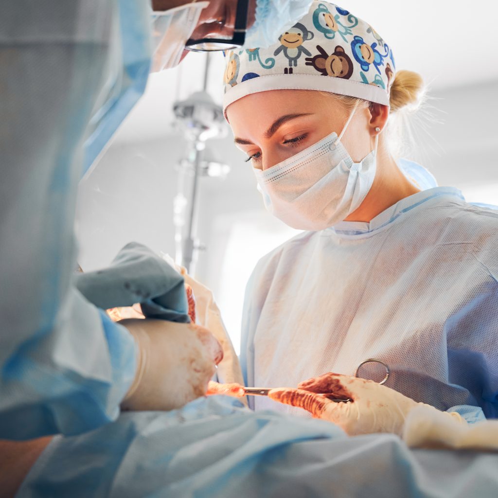 Doctors performing abdominoplasty surgery in clinic. Focus on female surgeon assistant wearing medical masks while doing abdominal plastic surgery in operating room. Concept of aesthetic surgery.
